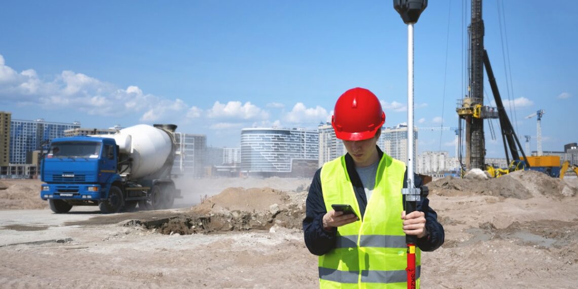 Agrimensor con chaleco reflectante y receptor GNSS en una obra